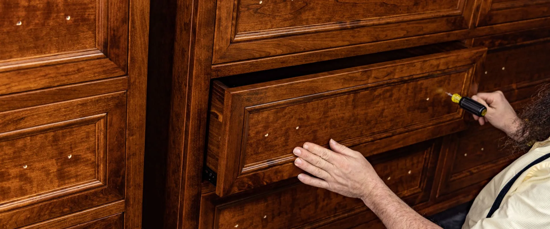 Criswell Furniture customizations with craftsman installing hardware on a hardwood drawer unit